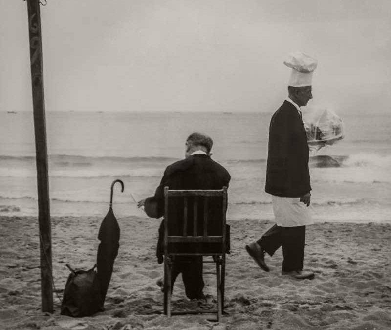 Fotografía de un caballero sentado y un camarero caminando junto al mar